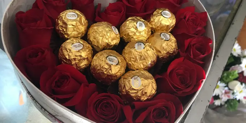 9 chocolates ferrero con rosas rojas al rededor en una caja de corazón