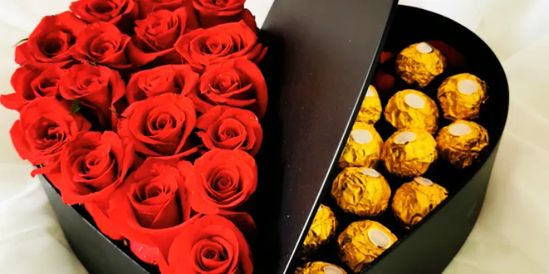 rosas rojas en caja de corazón negro junto a chocolates 